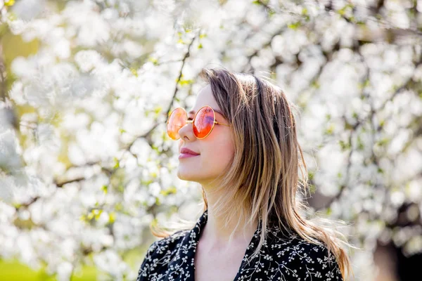 Bir güneş gözlüğü genç kız çiçekli bir ağacın yakınında kalmak — Stok fotoğraf