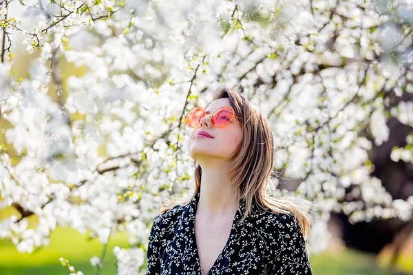 Bir güneş gözlüğü genç kız çiçekli bir ağacın yakınında kalmak — Stok fotoğraf