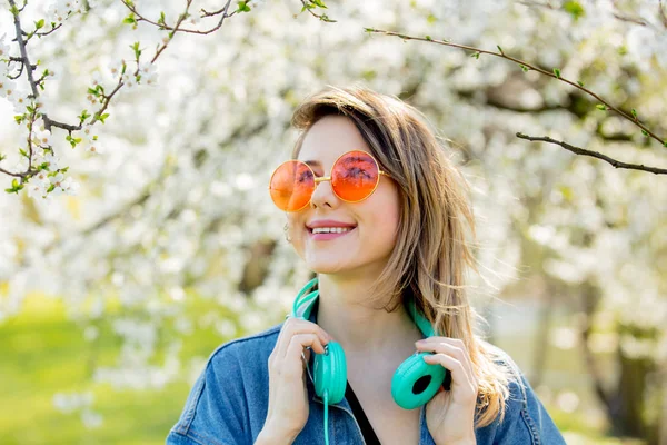 Fille dans une veste en denim et écouteurs près d'un arbre à fleurs — Photo