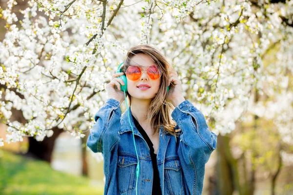 Fille dans une veste en denim et écouteurs près d'un arbre à fleurs — Photo