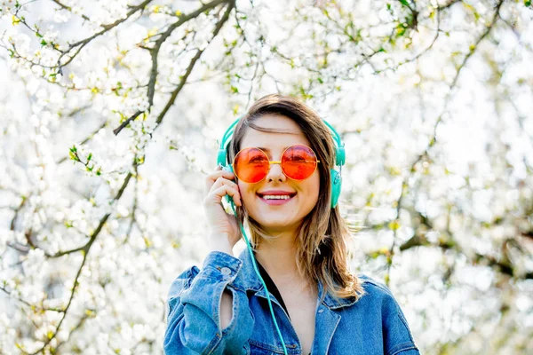 Meisje in een denim jas en koptelefoon in de buurt van een bloeiende boom — Stockfoto