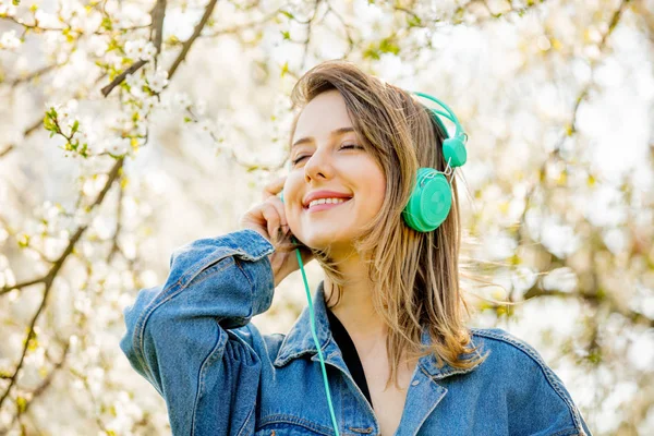 Flicka i en jeans jacka och hörlurar står nära en blommande tr — Stockfoto