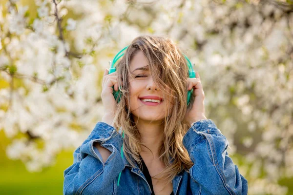 Girl in a denim jacket and headphones stands near a flowering tr — Stock Photo, Image