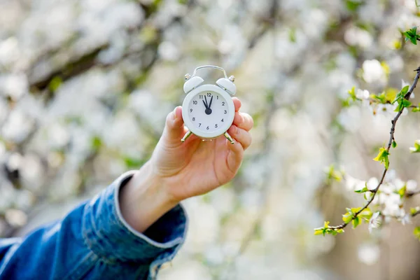 Kvinnlig hand håller väckar klocka nära blommande träd — Stockfoto