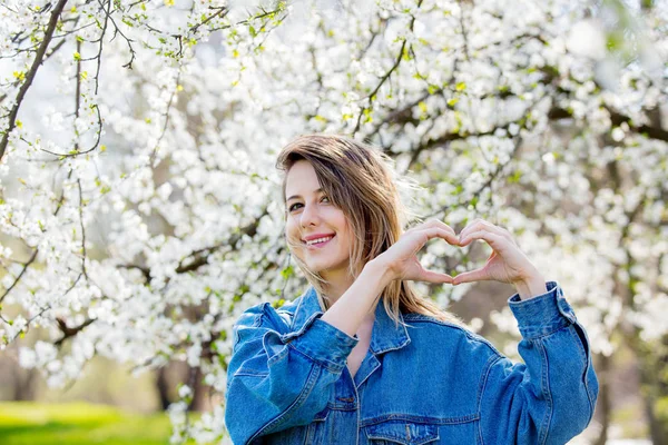 Chica en una chaqueta de mezclilla se encuentra cerca de un árbol con flores y mostrar hea —  Fotos de Stock