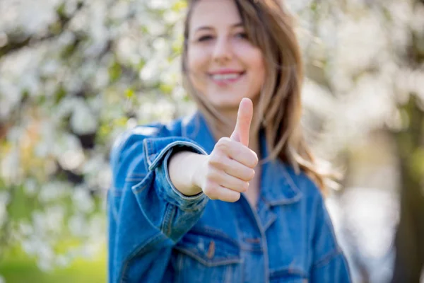 Meisje in een denim jas staat in de buurt van een bloeiende boom en Toon OK — Stockfoto