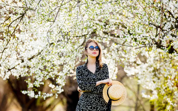 Młoda dziewczyna w okulary i kapelusz pobyt w pobliżu kwitnące drzewo — Zdjęcie stockowe