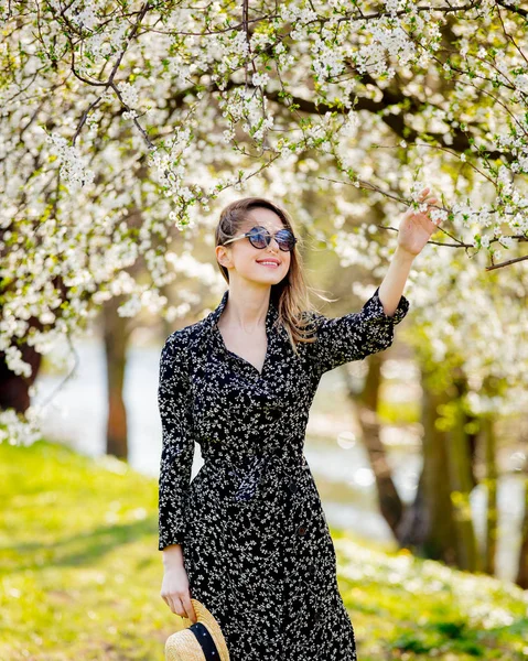 Mladá dívka v slunečních brýlích a v klobouku u kvetoucího stromu — Stock fotografie