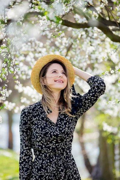 Jong meisje in een hoed verblijf in de buurt van een bloeiende boom — Stockfoto
