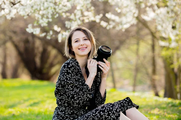 Ung flicka med kamera sitter nära en blommande träd i — Stockfoto