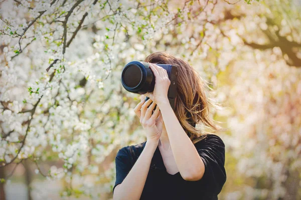 Chica joven con cámara de estancia cerca de un árbol de flores — Foto de Stock