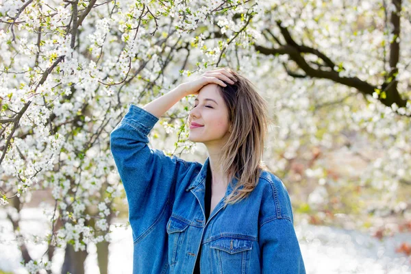 Flicka i en denim jacka bo nära en blommande träd — Stockfoto