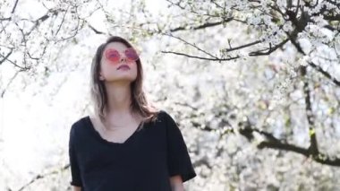 Bir güneş gözlüğü genç kız parkta bir çiçekli ağacın yakınında kalmak. Bahar sezonu