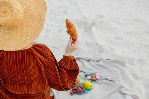 Młoda kobieta z rogalikiem je lunch na miotle na plaży — Zdjęcie stockowe