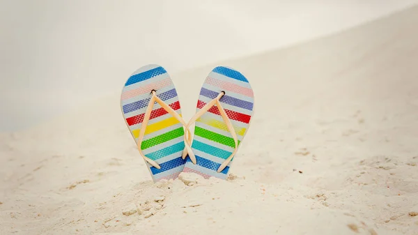 Beyaz kum üzerinde renkli çizgili parmak arası terlik ayakkabılar. — Stok fotoğraf