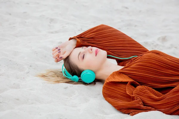 Νεαρή γυναίκα σε μπορντό χρώμα μπλούζα με ακουστικά ξαπλωμένη — Φωτογραφία Αρχείου