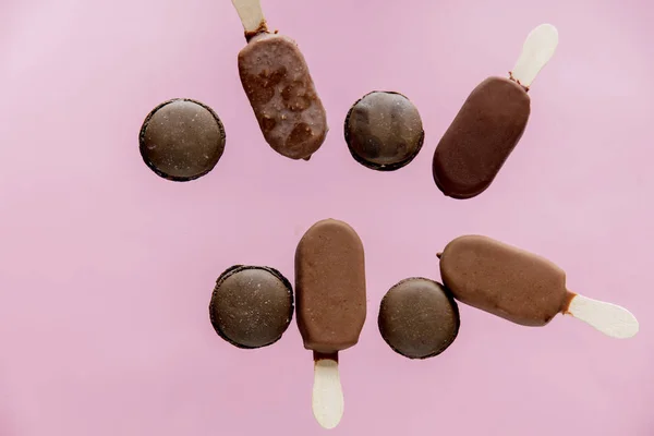 Chocolate ice lollys and french macrons on pink background. — Stock Photo, Image