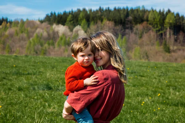 Mãe e filho no gramado do campo com montanhas e floresta — Fotografia de Stock
