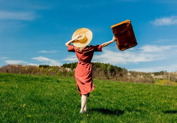 草原にスーツケースと赤いドレスと帽子の美しい女の子 — ストック写真