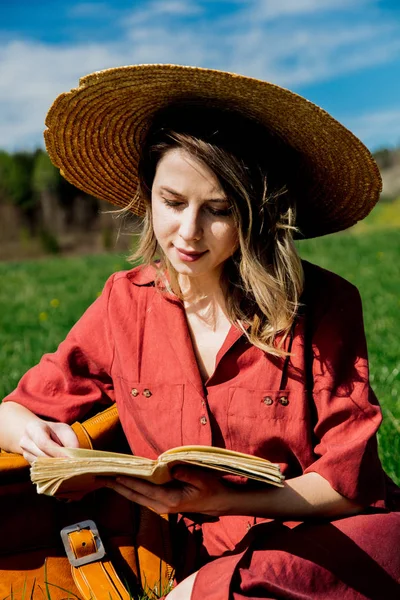 Mooi meisje in rode jurk en muts met koffer en boek zaten — Stockfoto