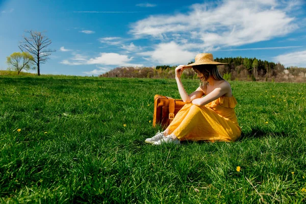 山の牧草地の機知に座っている黄色のドレスとスーツケースの女の子 — ストック写真