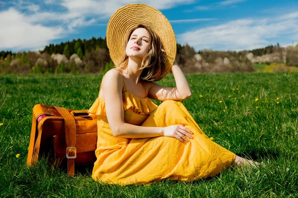 Chica en vestido amarillo y maleta sentado en el ingenio prado de montaña —  Fotos de Stock