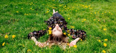 Genç kadın yeşil karahindiba çayırında uzanıyor.