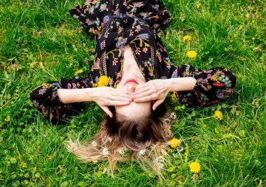 Genç kadın yeşil karahindiba çayırında uzanıyor.