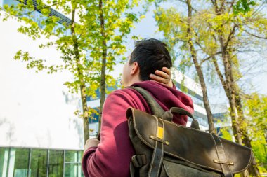 Sırt çantalı genç adam modern binanın yanındaki sokakta kalıyor.