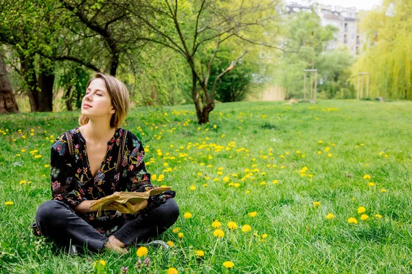 Ung kaukasisk kvinna med bok på äng med maskrosor. — Stockfoto