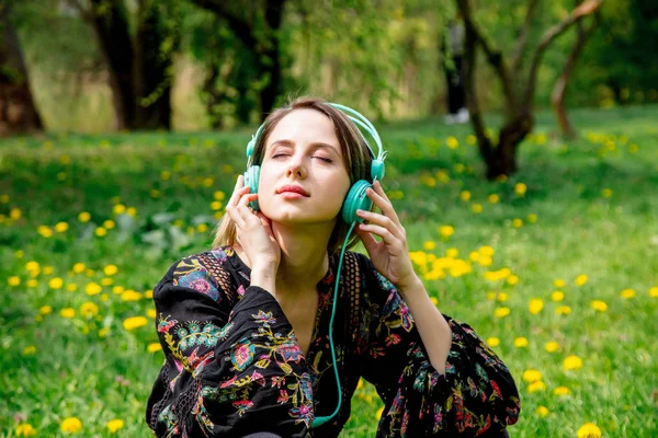 Jovem com fones de ouvido no prado de dente-de-leão verde no parque . — Fotografia de Stock