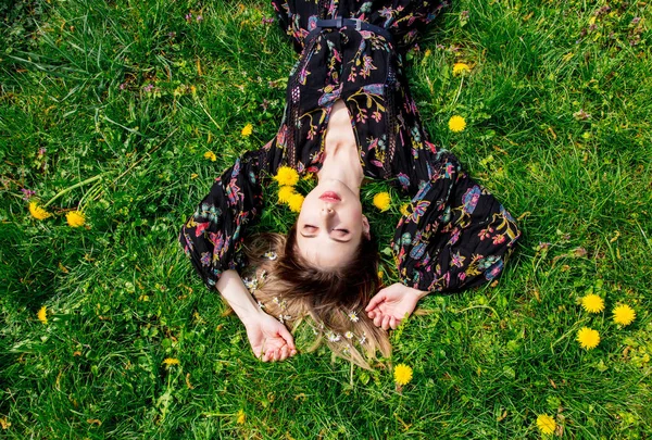 年轻女子躺在绿蒲公英的草地上 — 图库照片