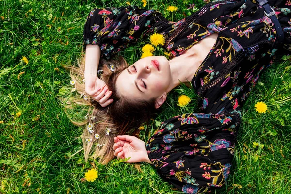 Young woman lying down on green dandelion meadow — Stock Photo, Image