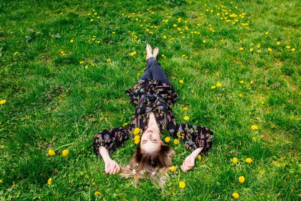Mladá žena ležící na zelené pampeliškové louce — Stock fotografie
