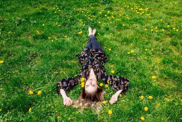 緑のタンポポの牧草地に横たわっている若い女性 — ストック写真