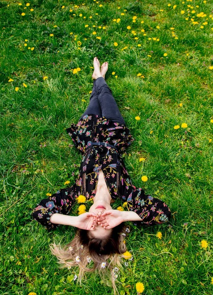 Genç kadın yeşil karahindiba çayırında uzanıyor. — Stok fotoğraf