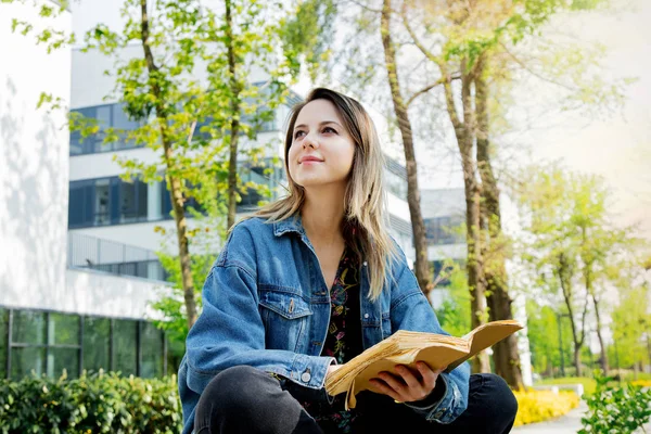 Jovem estudante em jaqueta jeans lendo um livro no beco perto — Fotografia de Stock