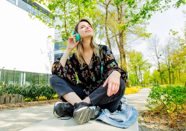 Junge Frau mit Kopfhörern sitzt in der Nähe moderner Univ-Gebäude — Stockfoto