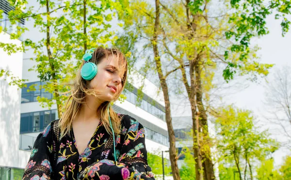 Jeune femme avec écouteurs assis près du bâtiment moderne de Univ — Photo