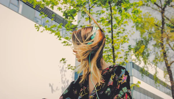 Mujer joven con auriculares sentado cerca de edificio moderno de Univ —  Fotos de Stock