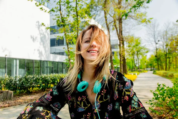 Junge Frau mit Kopfhörern sitzt in der Nähe moderner Univ-Gebäude — Stockfoto