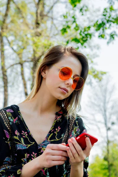 Młoda kobieta w okularach przeciwsłonecznych z telefonem komórkowym siedzi na zielono — Zdjęcie stockowe