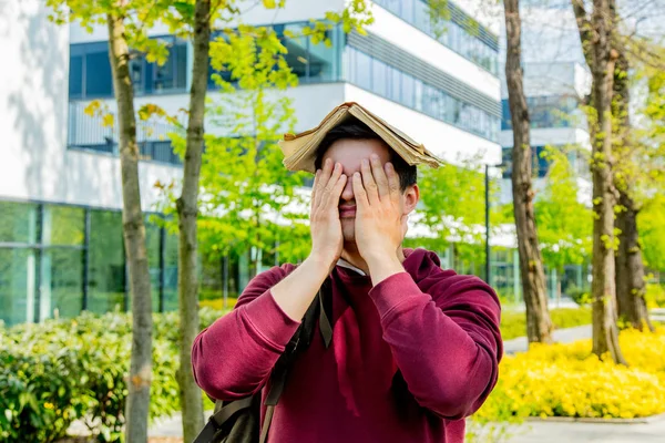 Jonge overstuur student met boek op hoofd verblijf in de buurt van modern gebouw — Stockfoto