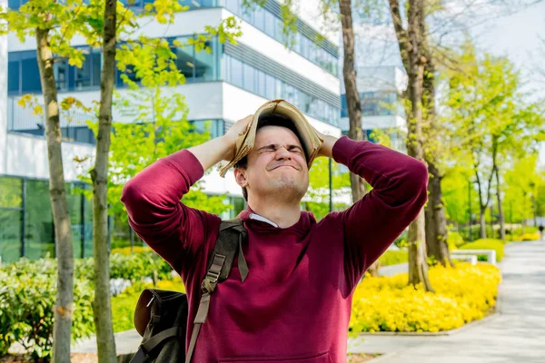Mladý naštvaný student s knihou o hlavu pobyt v blízkosti moderní budovy — Stock fotografie