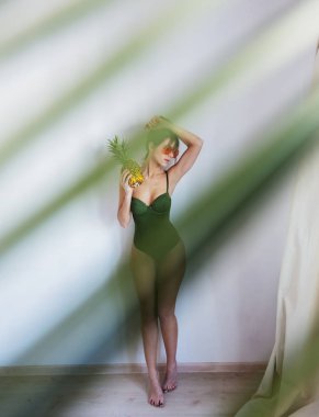 Female in bikini holding pineapple and with palm leaves[