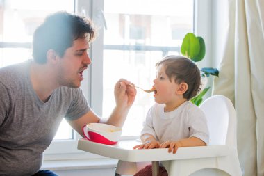 Genç baba küçük bir çocuğu çay kaşığıyla beslemeye çalışıyor.