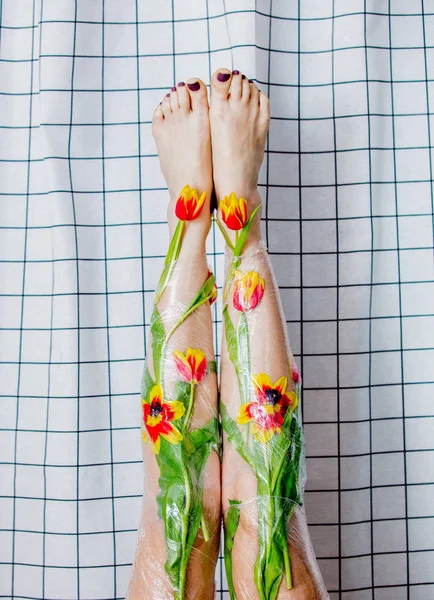 Nő tartja a lábát csomagolva celofán és virágok. — Stock Fotó