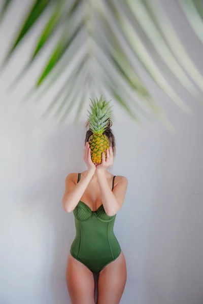 Жінка в зеленому купальнику тримає ананас з листям долоні — стокове фото
