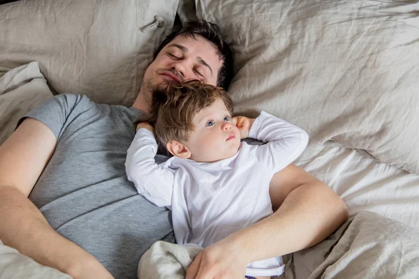 Молодий батько спить з маленьким хлопчиком, який вже прокинувся — стокове фото