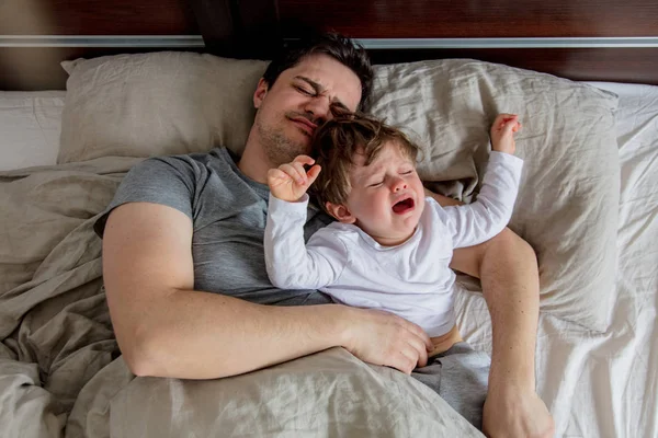 Молодий батько лежить у ліжку з плачучою дитиною — стокове фото
